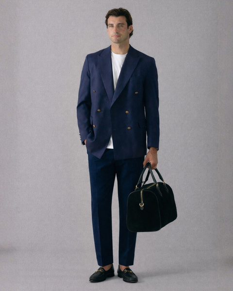 Man wearing a navy suit holding a black bag against a gray background