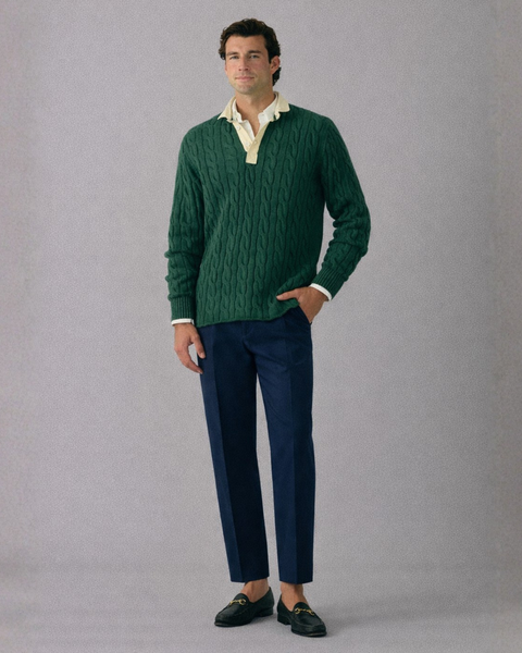 Man wearing a green sweater and blue pants against a gray background