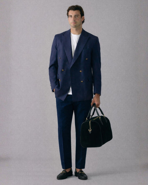 Man wearing a navy suit holding a black bag against a gray background