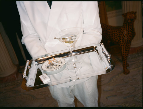 Person holding a tray with a glass of white wine and a small dish.