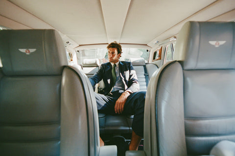 Man sitting in the back of a luxury vehicle with 'Bentley' logo on the seats.
