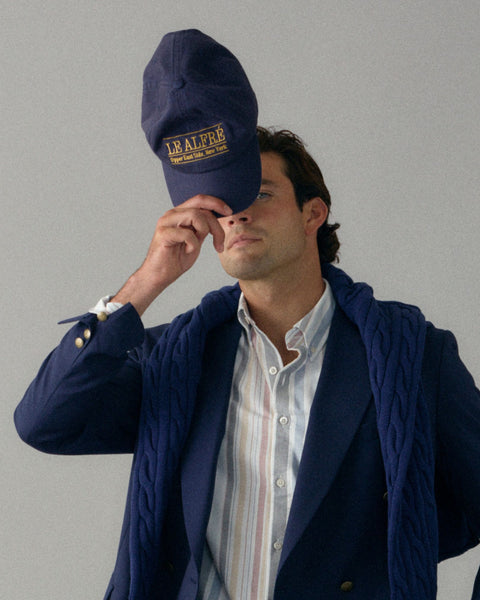 Man wearing a navy blue jacket and cap with a logo on a gray background
