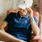 Person wearing a blue polo shirt and white bucket hat sitting on a floral-patterned couch.