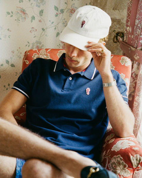 Person wearing a blue polo shirt and white bucket hat sitting on a floral-patterned couch.