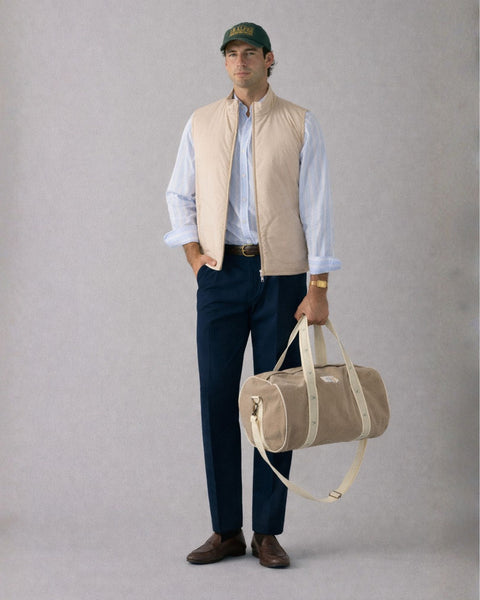 Man holding a beige duffel bag against a plain background