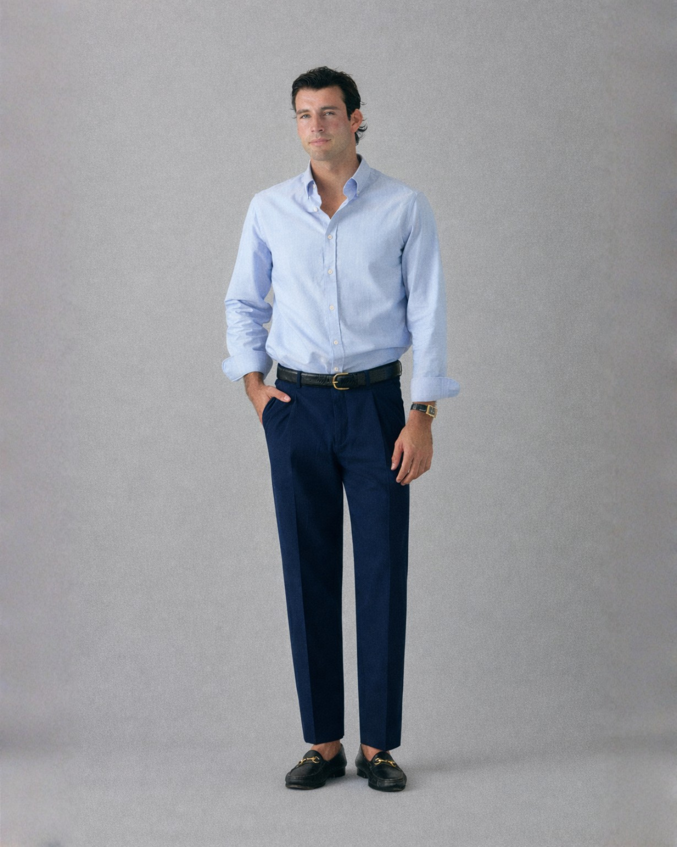 Man wearing a light blue shirt and dark blue pants against a gray background