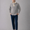 Man wearing a gray cable knit sweater, white shirt, blue pants, and black shoes on a gray background