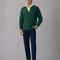Man wearing a green sweater and blue pants against a gray background
