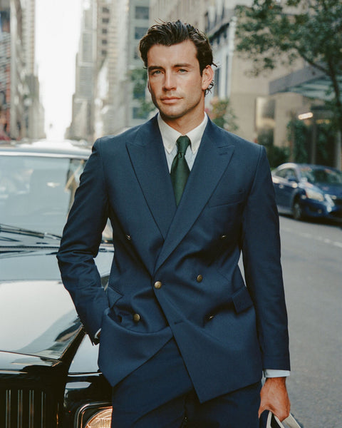 Man in a blue suit standing on a city street with cars and buildings in the background