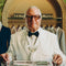 Man in a white suit holding a tray with a cocktail glass in a formal setting.